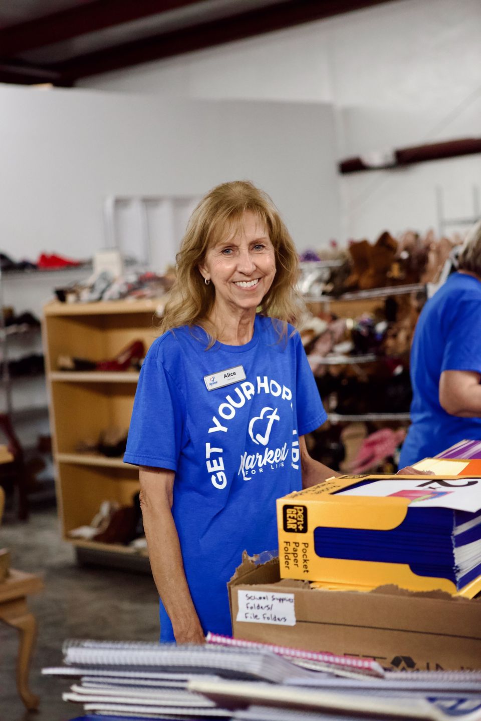 Alice, wearing a Marked For Life name badge, sorts pocket folders and notebooks for Back to School Outreach.